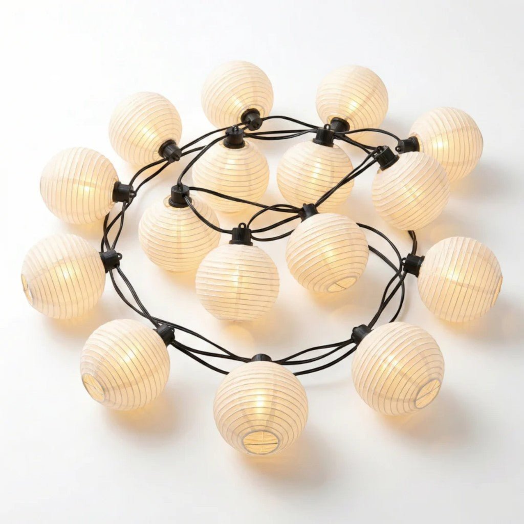 White lantern string lights loosely coiled on a white background, glowing softly, with black sockets and wire