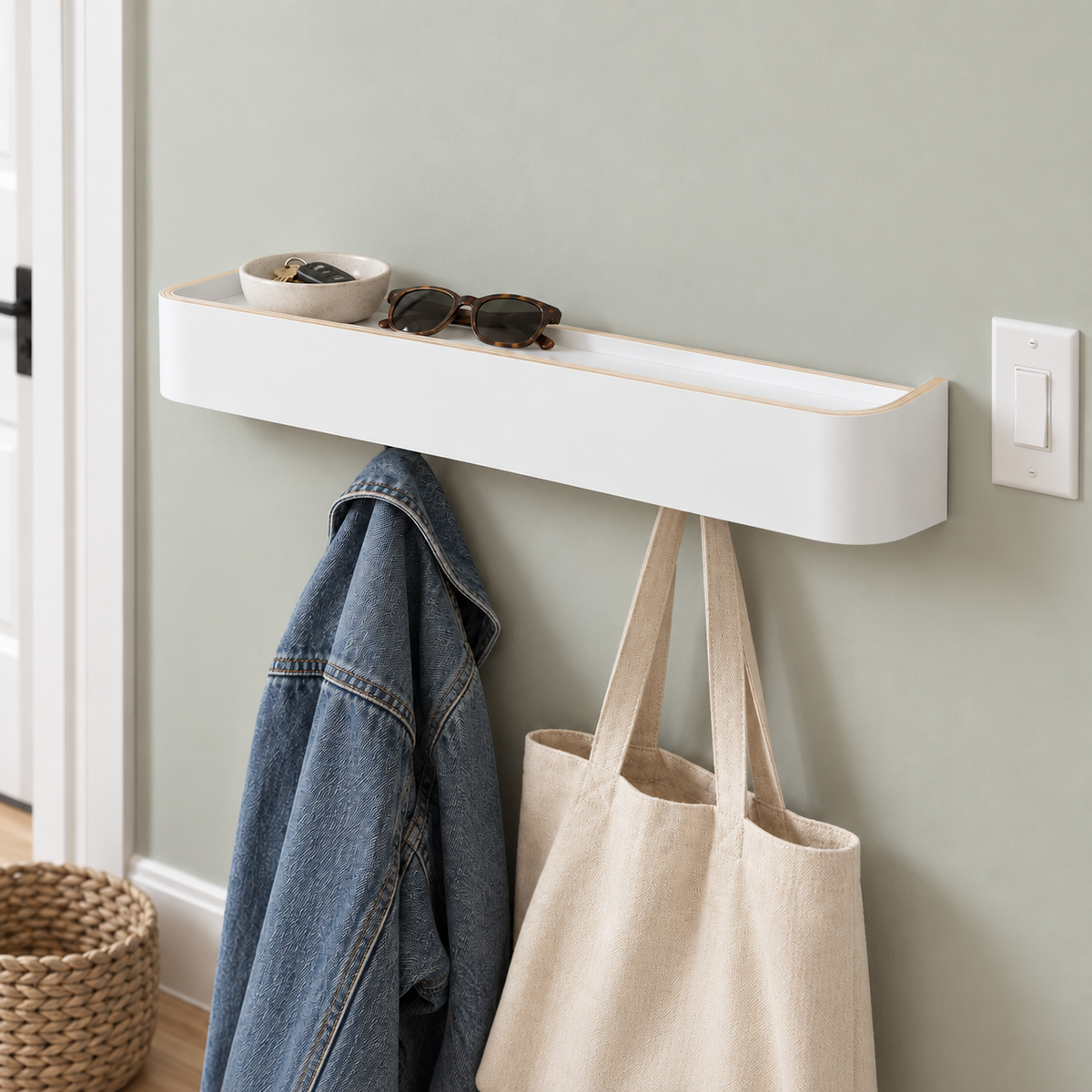 White wall coat rack with shelf on a pale sage wall by the door, a denim jacket and a canvas tote on the hooks