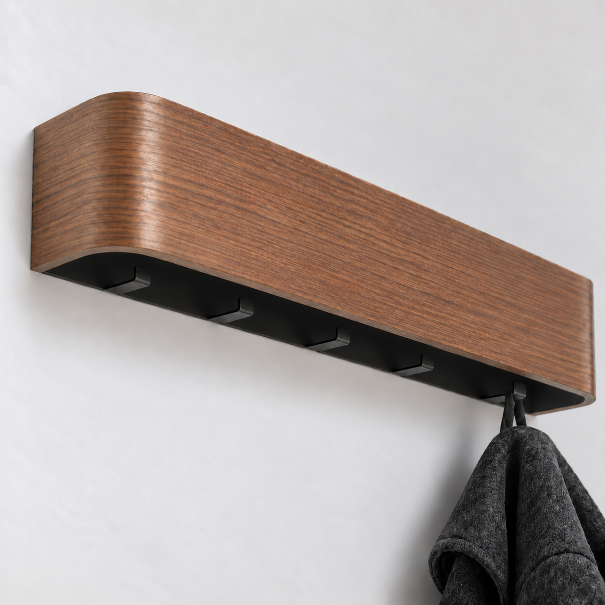 Close view under the walnut wall coat rack showing its five small black hooks, with a charcoal coat hanging from the last one
