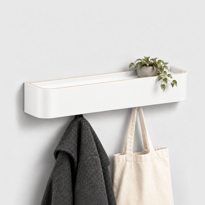 White wall coat rack with shelf, a small trailing plant in a gray pot on top and a charcoal coat and canvas tote bag hanging from the hooks underneath