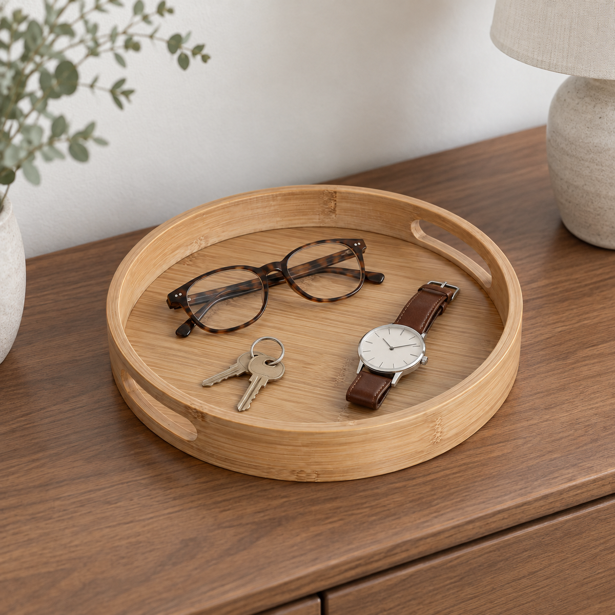 Small round bamboo tray on a walnut dresser holding a wristwatch, keys and folded reading glasses