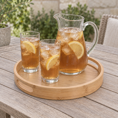 Round bamboo tray carrying a glass pitcher of iced tea and two tall glasses on an outdoor table