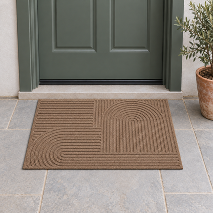 Brown grooved doormat with a raised arc pattern on a stone porch in front of a green-gray front door