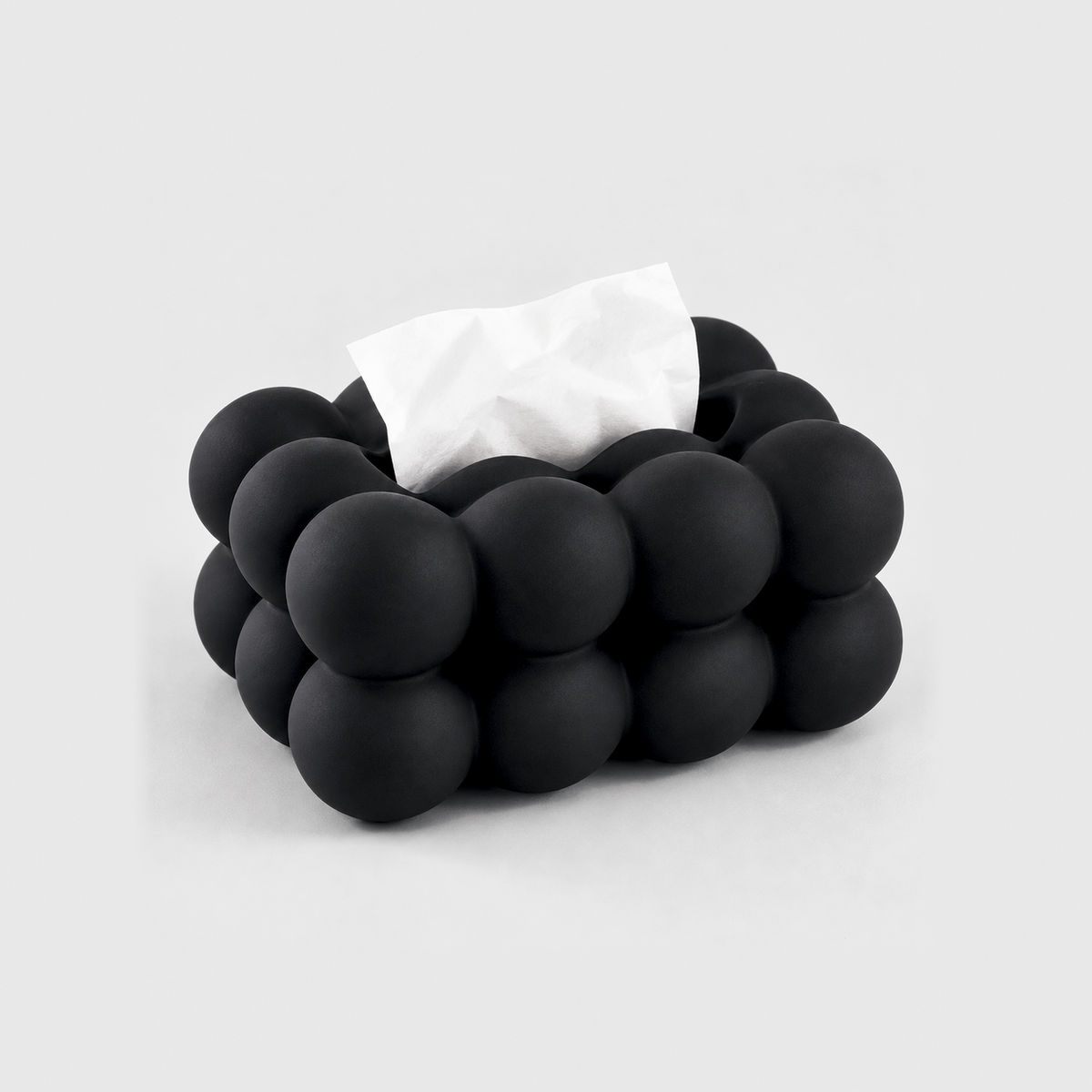 Black bubble tissue box cover in matte ceramic with a tissue in its top slot, on a light gray background