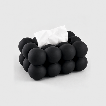 Black bubble tissue box cover in matte ceramic with a tissue in its top slot, on a light gray background