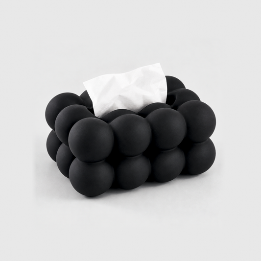 Black bubble tissue box cover in matte ceramic with a tissue in its top slot, on a light gray background