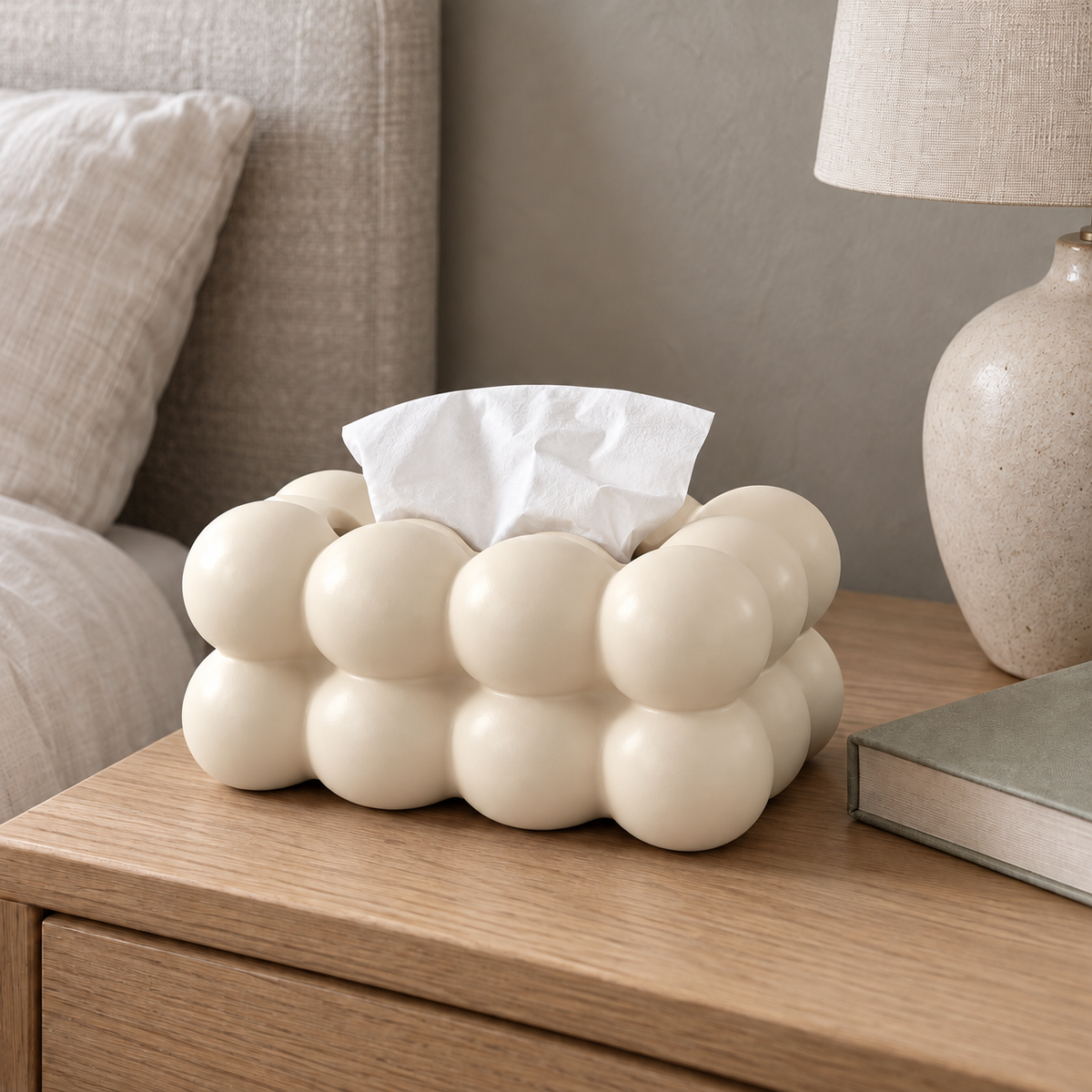 Cream bubble tissue box cover on an oak nightstand next to a table lamp and a book