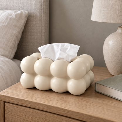 Cream bubble tissue box cover on an oak nightstand next to a table lamp and a book