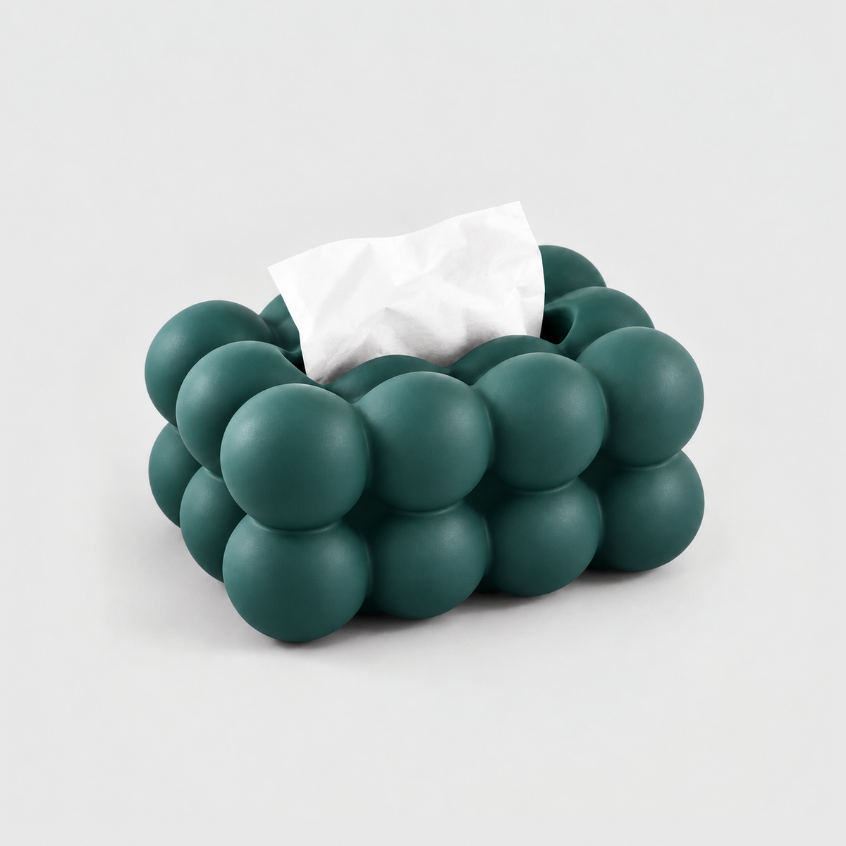 Teal bubble tissue box cover in matte ceramic with a tissue in its top slot, on a light gray background