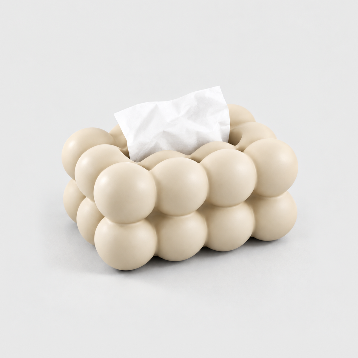 Cream bubble tissue box cover in matte ceramic with a tissue in its top slot, on a light gray background