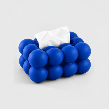 Blue bubble tissue box cover in matte ceramic with a tissue in its top slot, on a light gray background