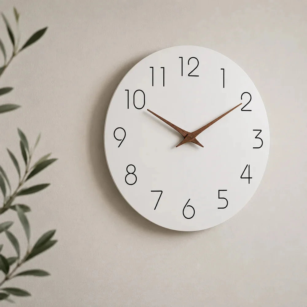 The white wall clock seen at an angle on a light wall, with a green olive branch at the left