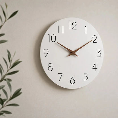 The white wall clock seen at an angle on a light wall, with a green olive branch at the left