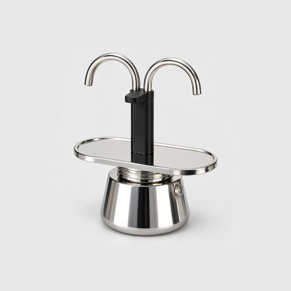 Mini moka pot with a dual spout, black center column and polished stainless steel base and cup tray, on a light gray background