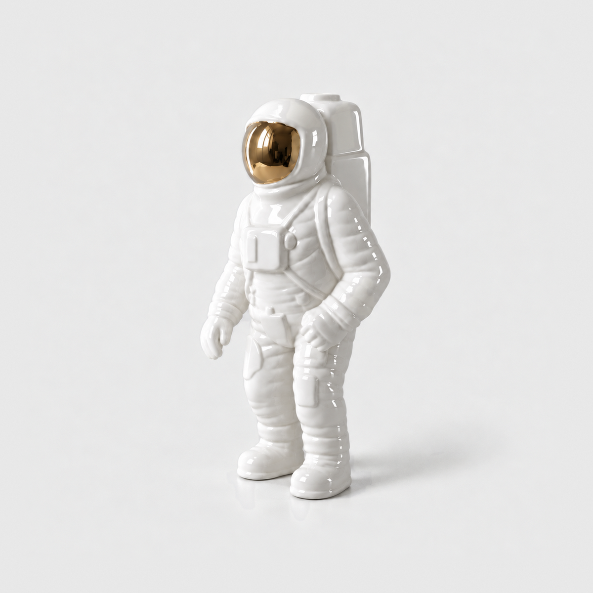 A white ceramic astronaut vase with a gold visor and a backpack opening, standing on a light gray background