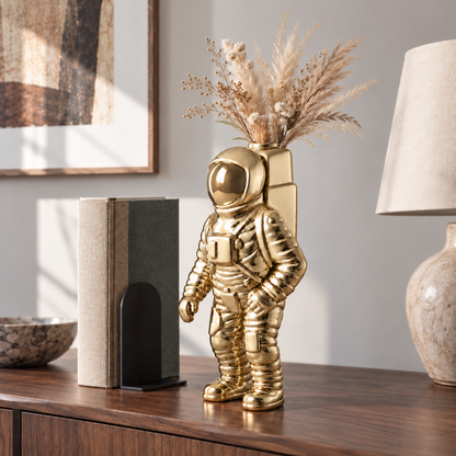 A mirror gold astronaut vase with dried grass in its backpack on a walnut sideboard in a living room