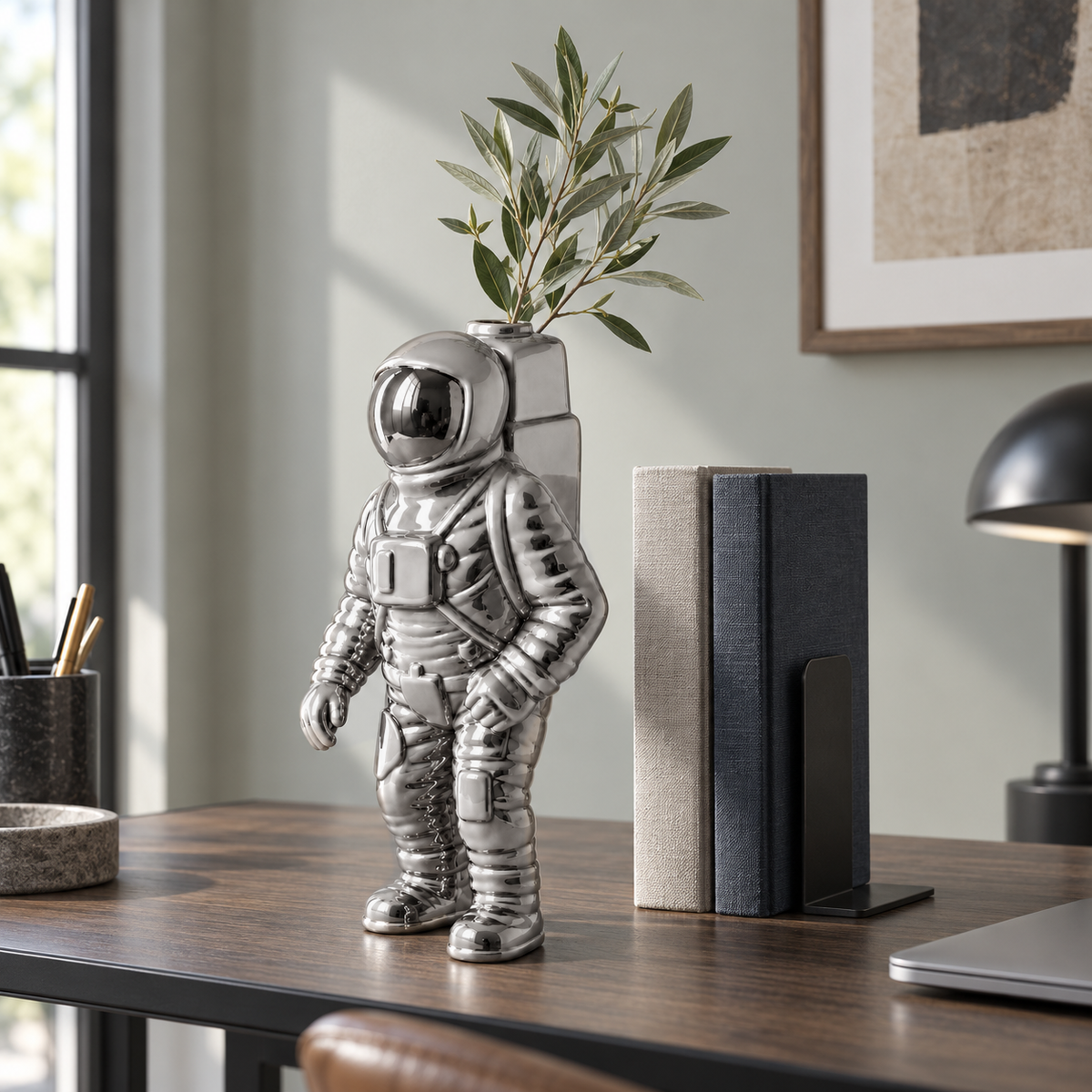 A mirror silver astronaut vase holding an olive branch on a black and oak desk in a home office