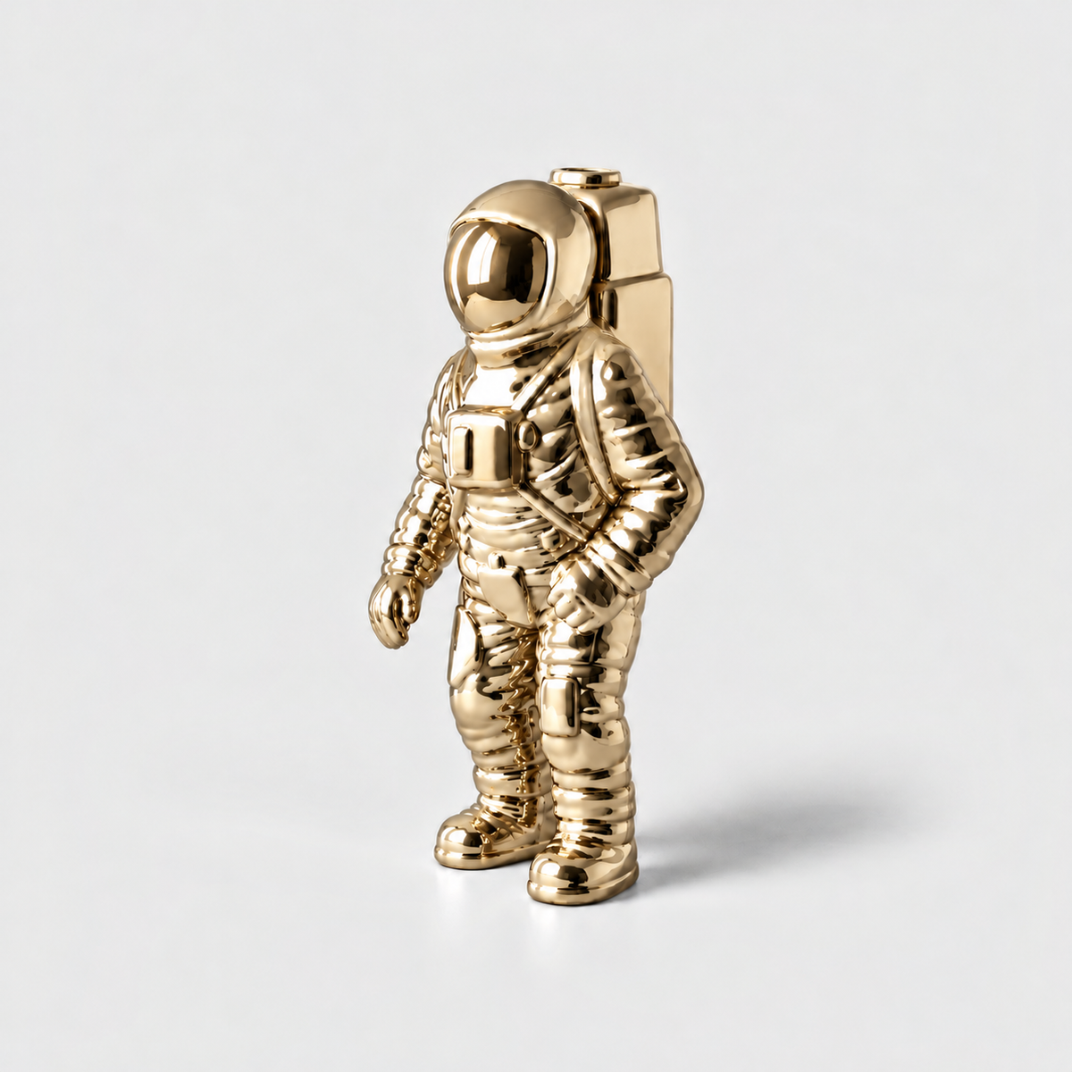 A mirror gold ceramic astronaut vase with a backpack opening, standing on a light gray background