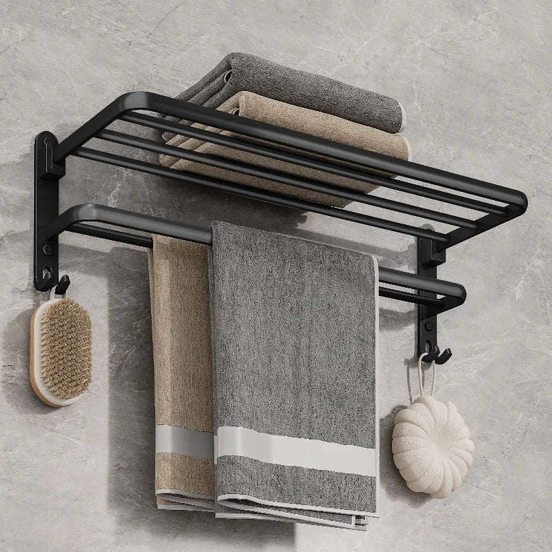 Matte black folding towel rack on a gray marble wall with folded towels on the top shelf, two towels on the bar and a brush and sponge on the hooks