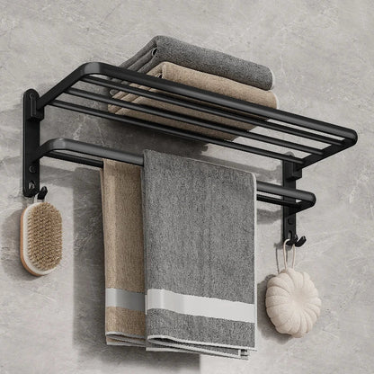 Matte black folding towel rack on a gray marble wall with folded towels on the top shelf, two towels on the bar and a brush and sponge on the hooks