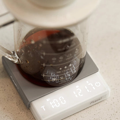 White coffee scale seen from above under a glass server and dripper, the display showing pour-over mode, time and weight