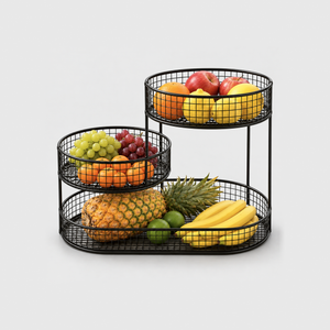 Black 3 tier fruit basket stand with an oval wire base and two round baskets stepped above it, filled with pineapple, bananas, grapes, oranges, lemons and apples, on a plain light gray background