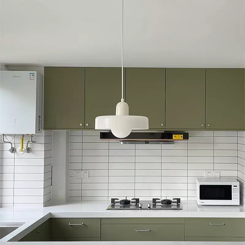 White glass pendant light with a beige body hanging over a kitchen with green cabinets and white tiles