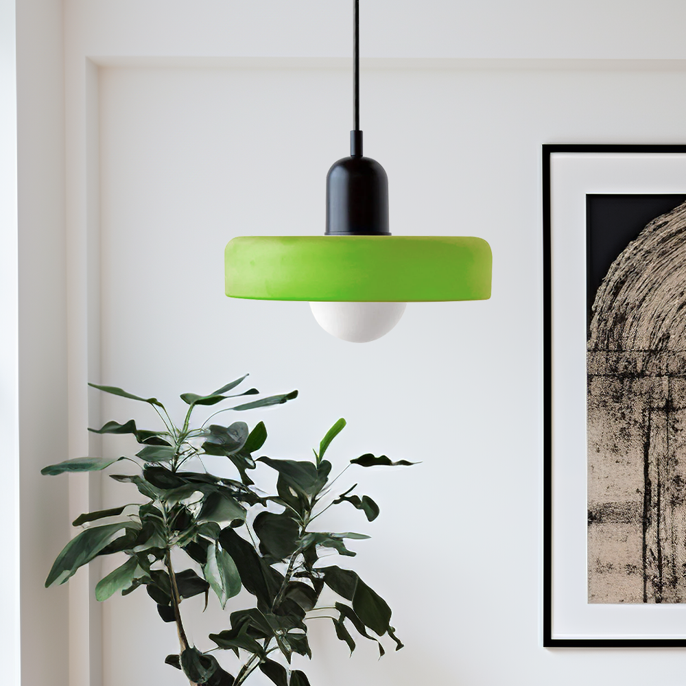 Bright green glass ring pendant with a black body in a white room beside a plant and a framed print