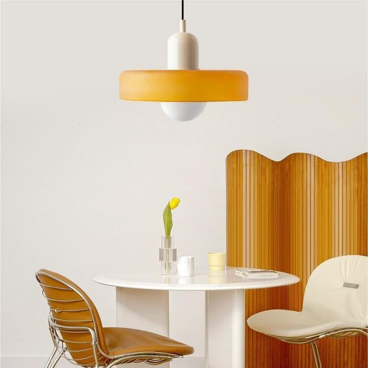 Amber glass pendant light with a beige body over a small round table and curved chairs