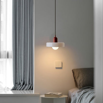White glass pendant with a burgundy body glowing warm over a bedside table in a gray bedroom