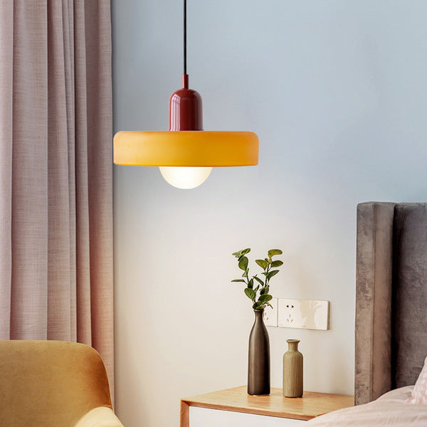 Amber glass pendant with a burgundy body beside a bed and a small side table with vases