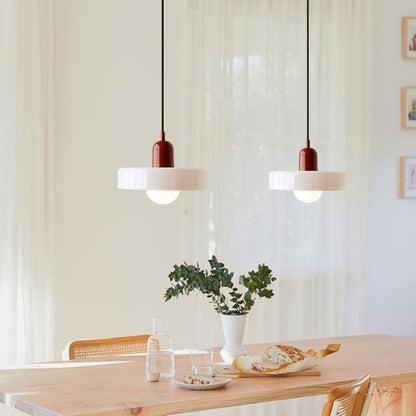 Two white glass pendants with burgundy bodies above a light wooden table with flowers