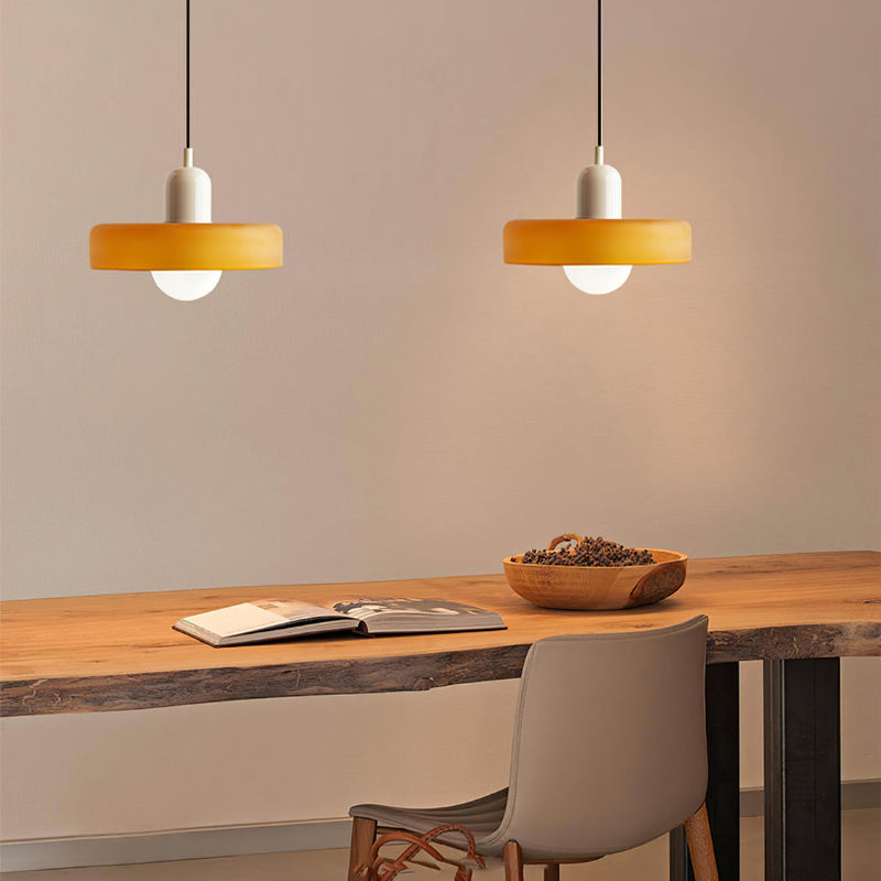Two amber glass pendants with beige bodies hanging over a live edge wooden desk