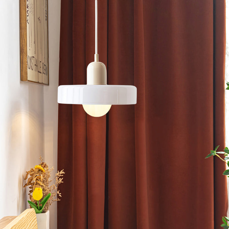 White glass ring pendant with a beige body and white cord in front of rust colored curtains