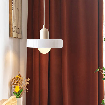 White glass ring pendant with a beige body and white cord in front of rust colored curtains