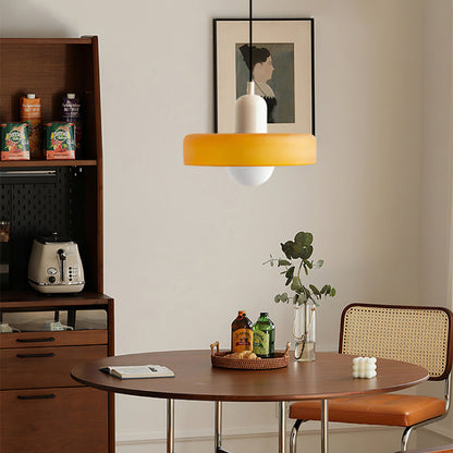 Amber glass pendant light with a beige body over a round walnut dining table and cane chairs