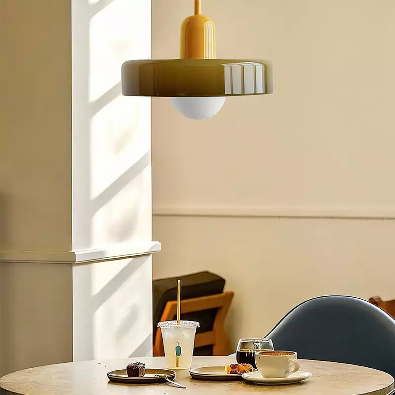 Olive glass pendant with a yellow body above a café table with coffee and pastries in sunlight