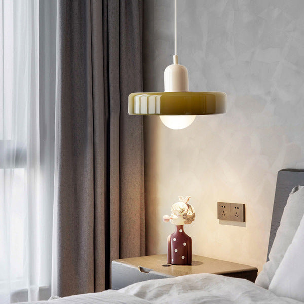 Olive glass pendant with a beige body hanging beside a bed and a nightstand