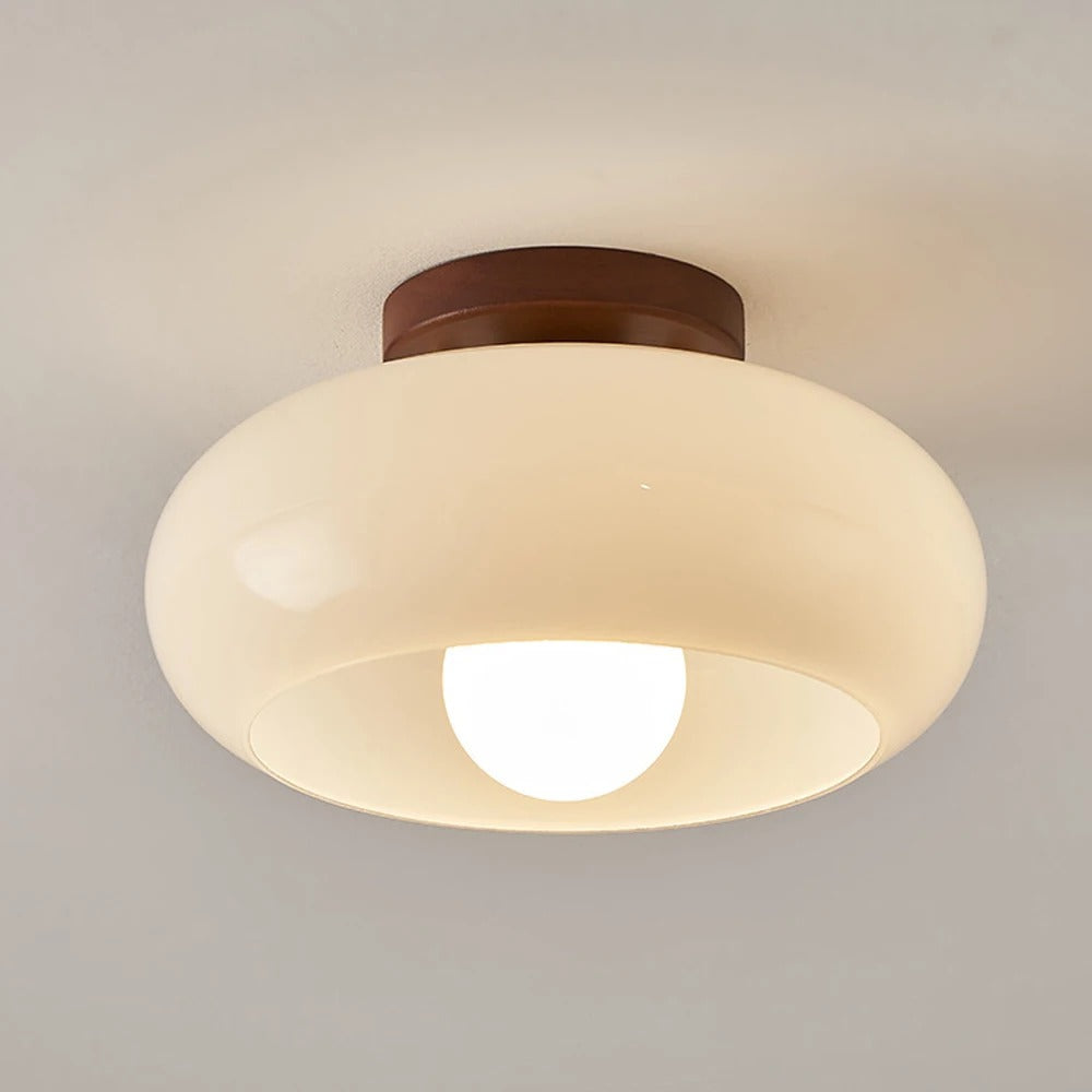 Bauhaus-style flush ceiling light with a rounded cream glass shade on a round brown base, lit, against a plain pale ceiling