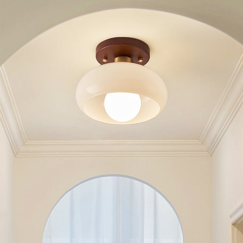 Cream glass flush mount light glowing warm on the arched ceiling of a white hallway
