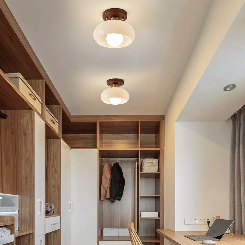 Two cream glass ceiling lights in a row along the ceiling of a walk-in closet corridor with wood wardrobes