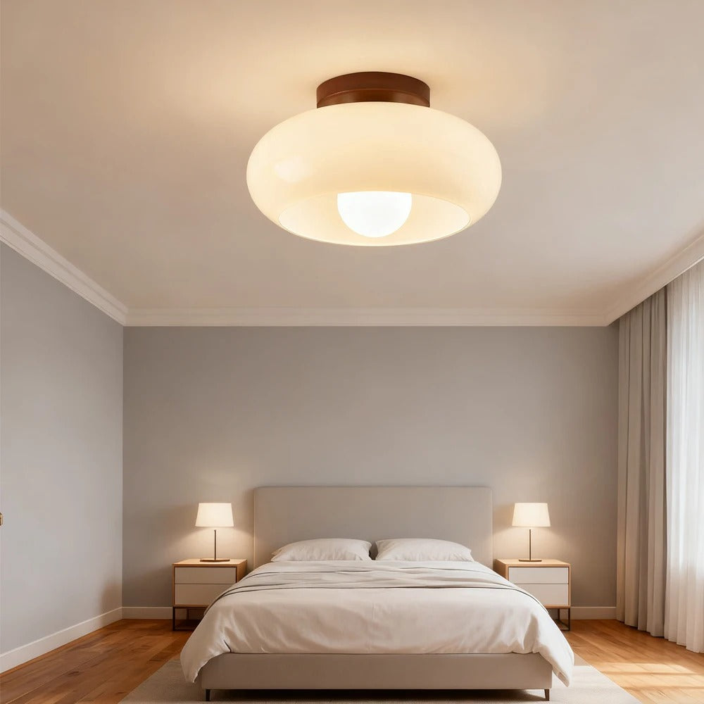 Cream glass flush ceiling light lit above a made double bed with two bedside lamps
