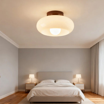 Cream glass flush ceiling light lit above a made double bed with two bedside lamps