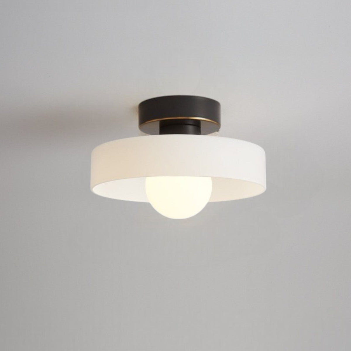 Bauhaus ceiling light with a white glass disc shade on a black ceiling base, a frosted globe glowing beneath it