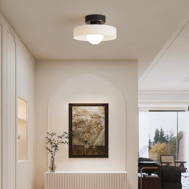 White glass ceiling light on a black base lighting a cream hallway with an arched niche and a framed painting
