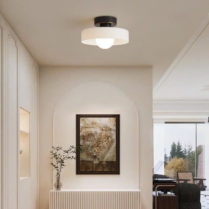 White glass ceiling light on a black base lighting a cream hallway with an arched niche and a framed painting
