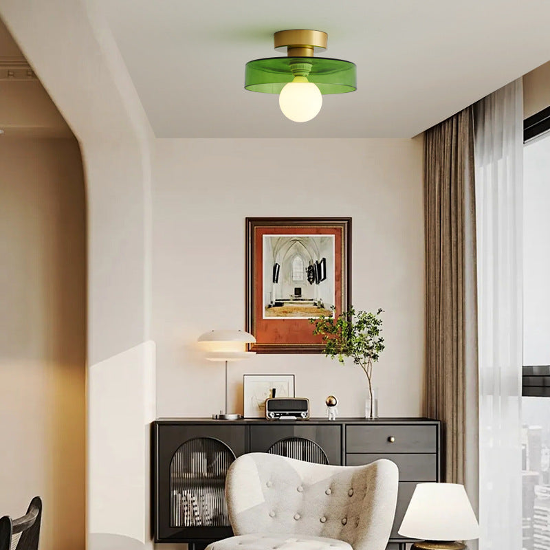 Green glass ceiling light on a gold base over a living room with a dark sideboard and a cream armchair