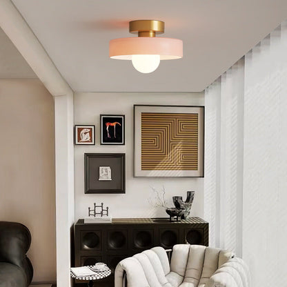 Pink glass ceiling light on a gold base over a sitting area with a gallery wall and a cream armchair