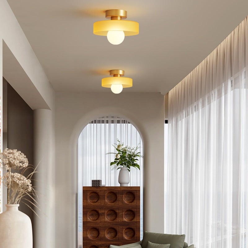 Two yellow glass ceiling lights on gold bases along a bright hallway leading to an arched window