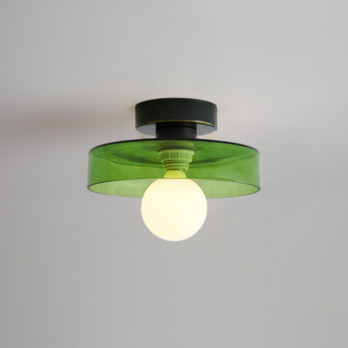 Ceiling light with a tinted green glass disc shade on a black base, lit from below by a frosted globe